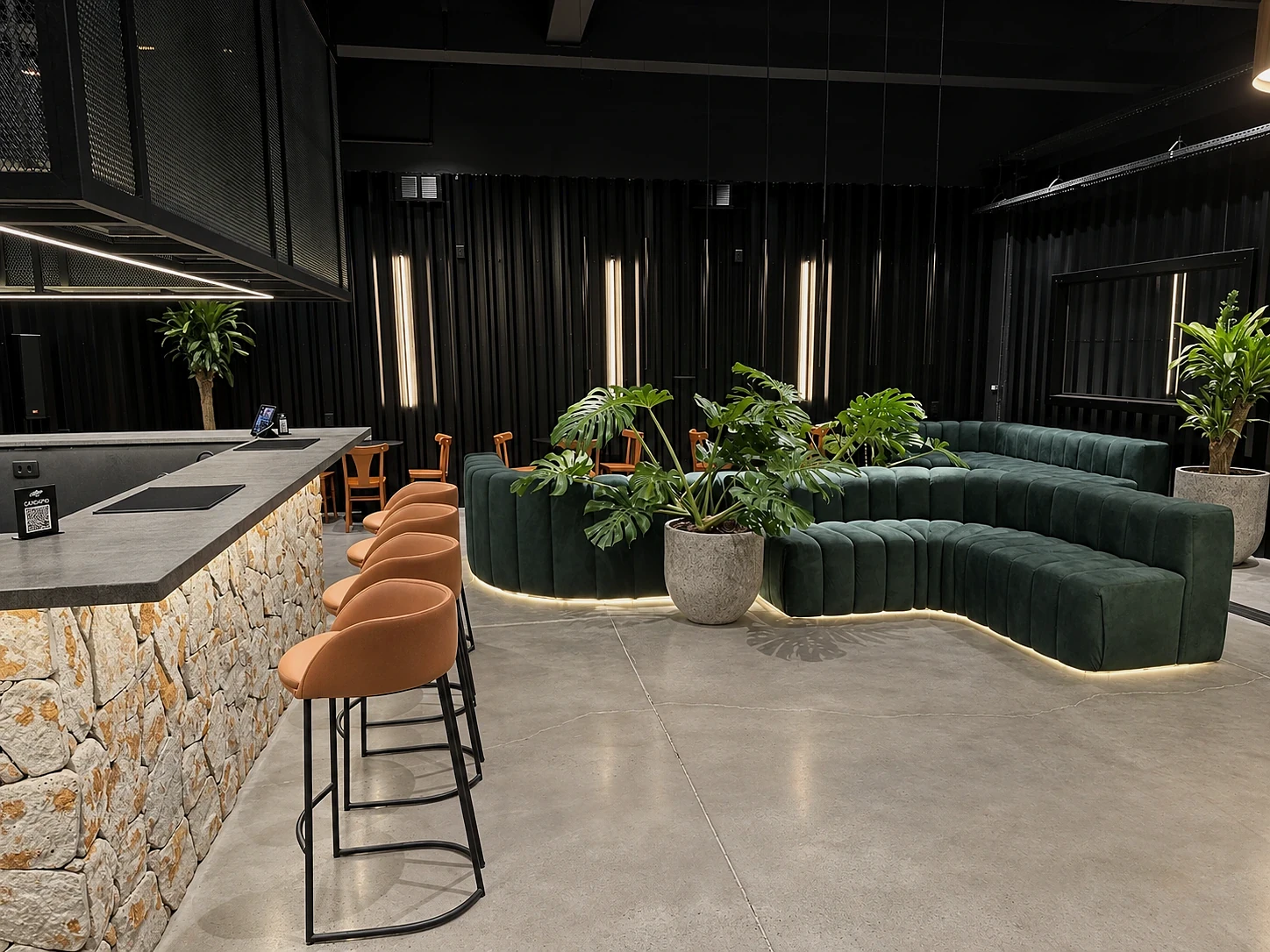 Vista geral do Baco Lounge com bar em pedra, sofás curvos e vegetação integrada.