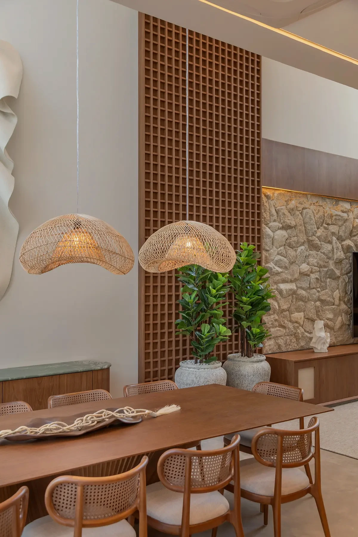 Sala de jantar da Casa Pequi com mesa de madeira, cadeiras trançadas e pendentes.